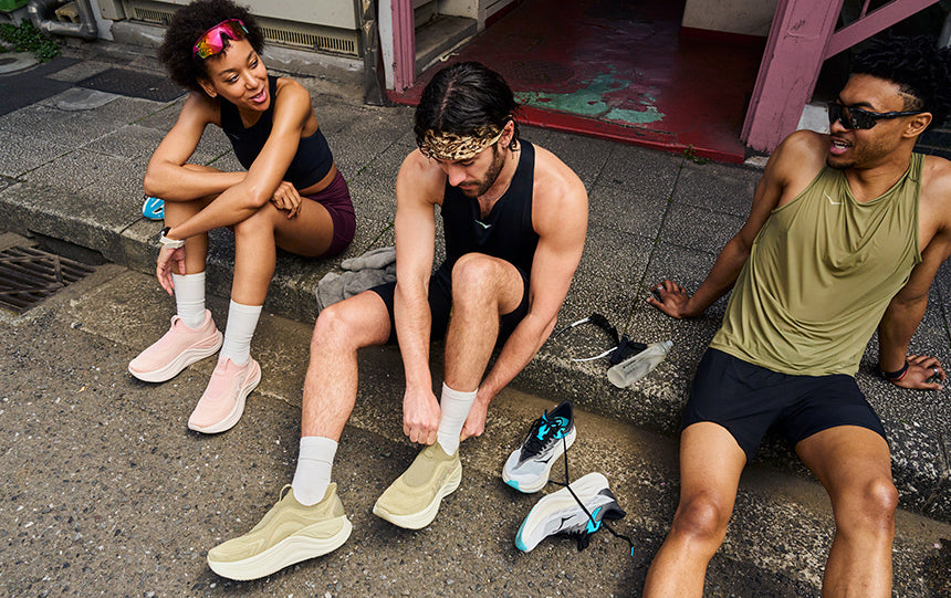 runners sitting on sidewalk changing into hoka skyward laceless recovery shoes post run.