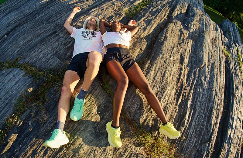 A man and a woman lying on a rock formation in HOKA Global Running Day shoes and clothing