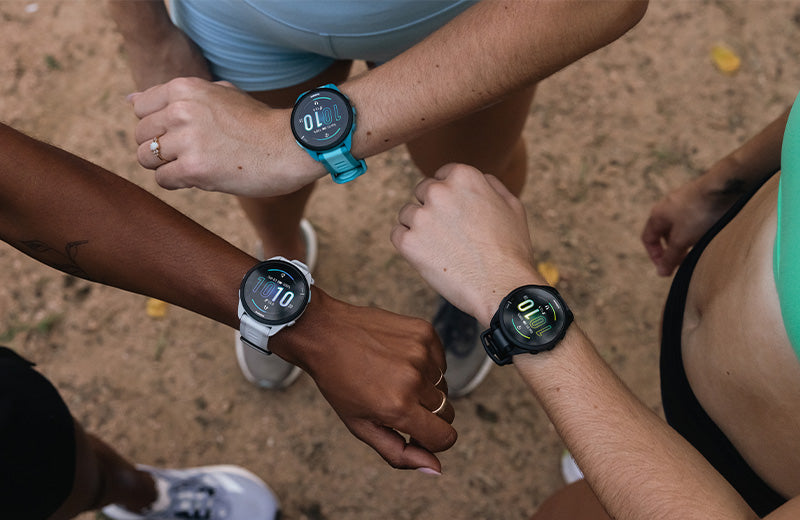 Downward view of three runners wearing differently colored Garmin GPS watches on their wrists.