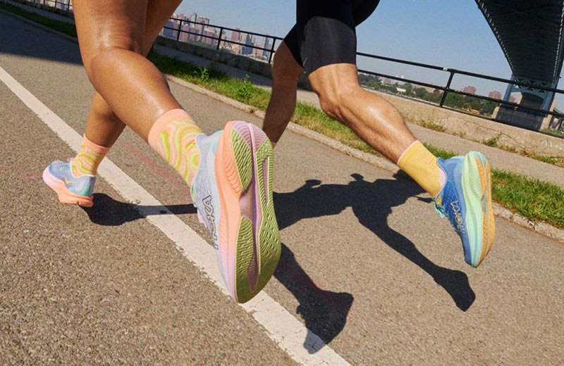 Lifestyle image: Two people running under a city overpass in men's and women's HOKA Mach 6 running shoes.