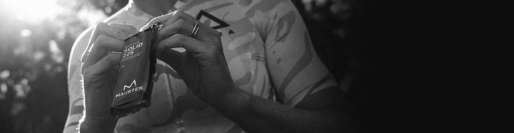 Black and white image of a cyclist opening a Maurten Solid 225 nutrition bar.