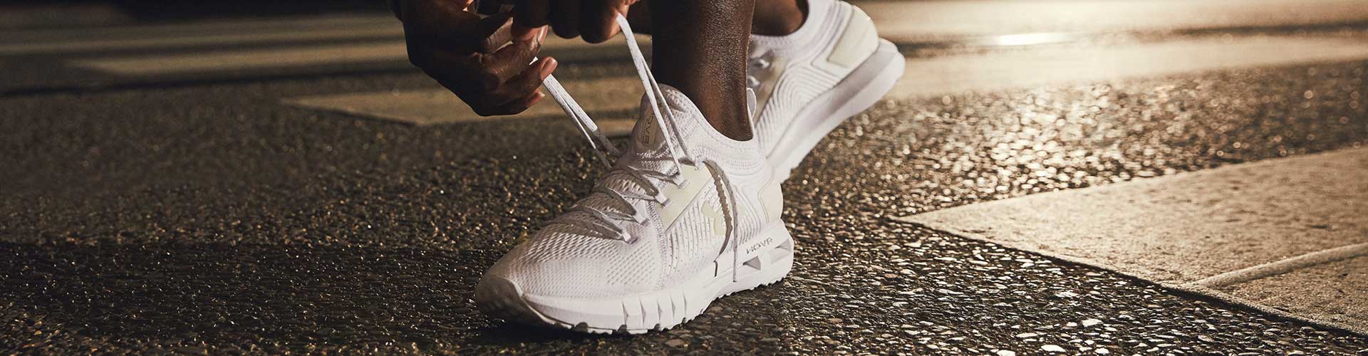 Man in white Under Armour running shoes tying up laces