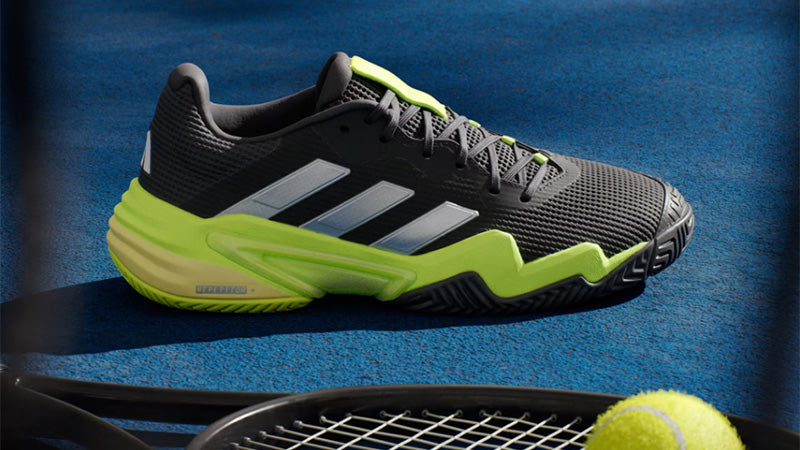 adidas barricade tennis shoes on tennis court with teniss ball