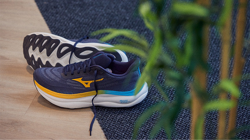 A pair of Mizuno Wave Sky 9 running shoes on a wooden floor with a plant in the foreground