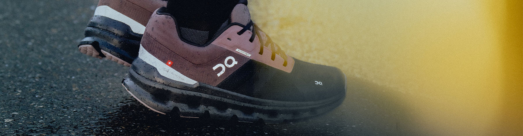 Closeup of a person wearing On Cloudrunner Waterproof running shoes on a wet pavement.