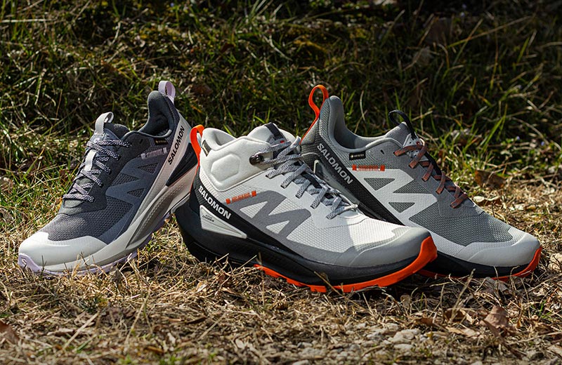 Three Salomon Elixir Activ GTX hiking shoes sitting on the ground, surrounded by green and brown vegitation