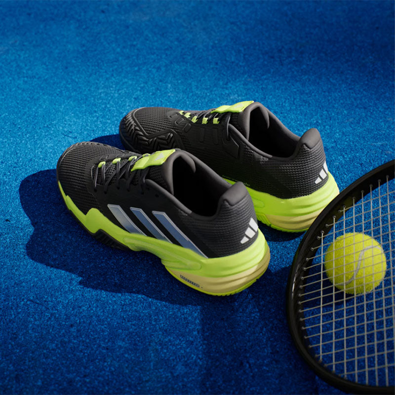 Black and yellow adidas Barricade 13 tennis shoes on a blue court