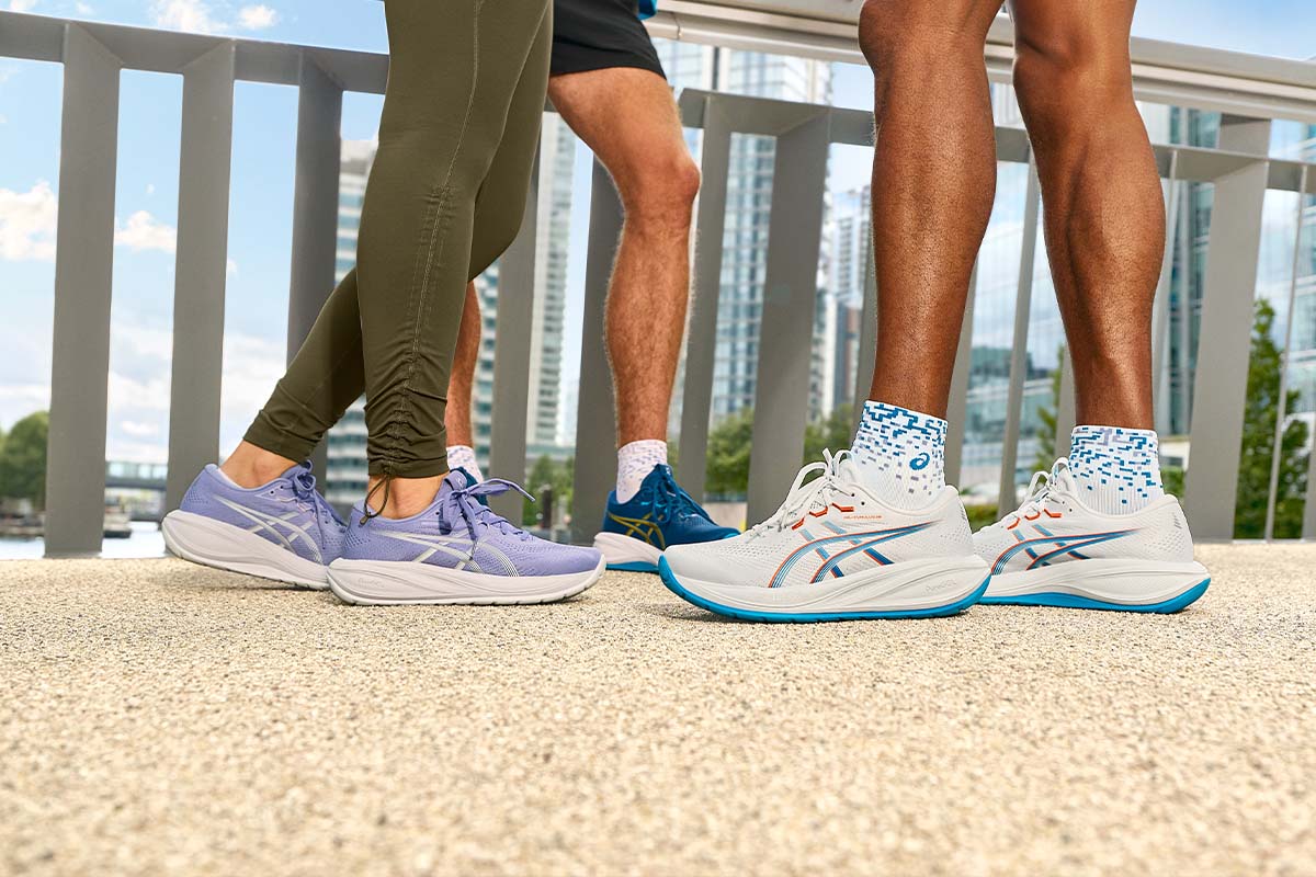 People wearing purple, blue and white ASICS GEL-Cumulus 28 women's and men's running shoes on a city sidewalk.