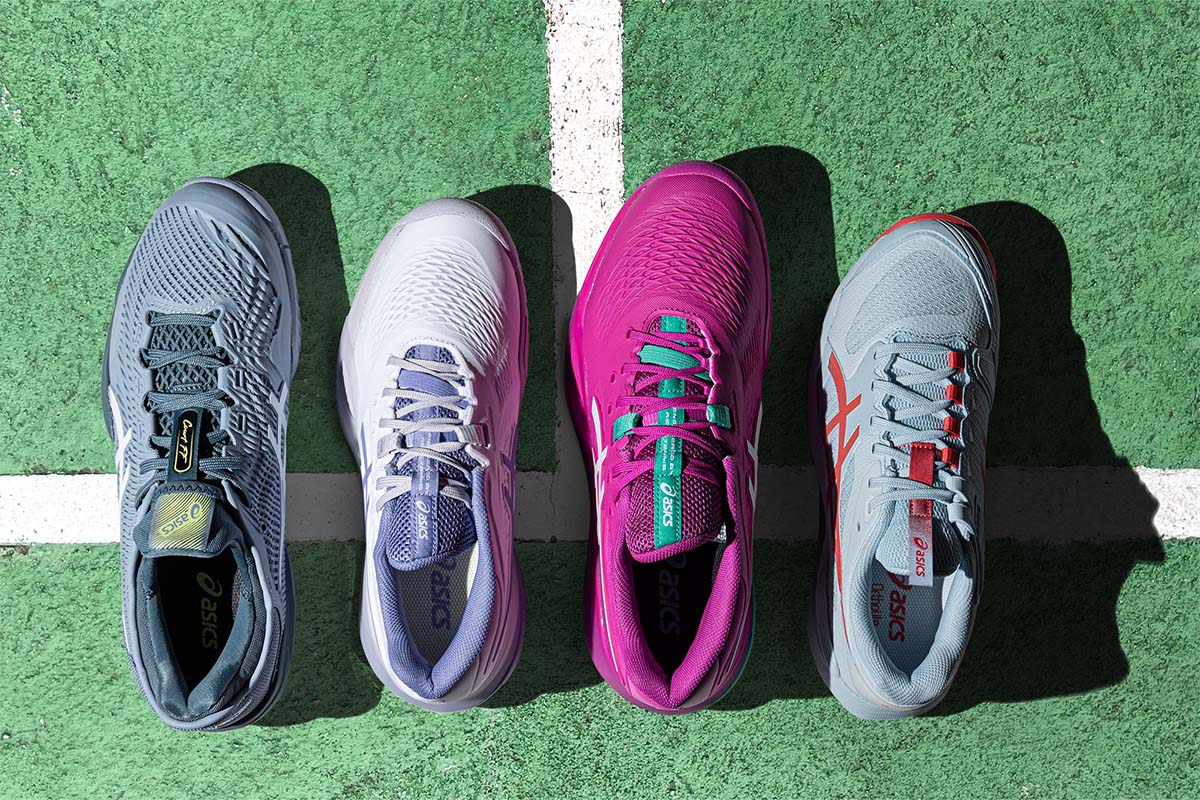 Four ASICS tennis shoes on a green tennis court surface