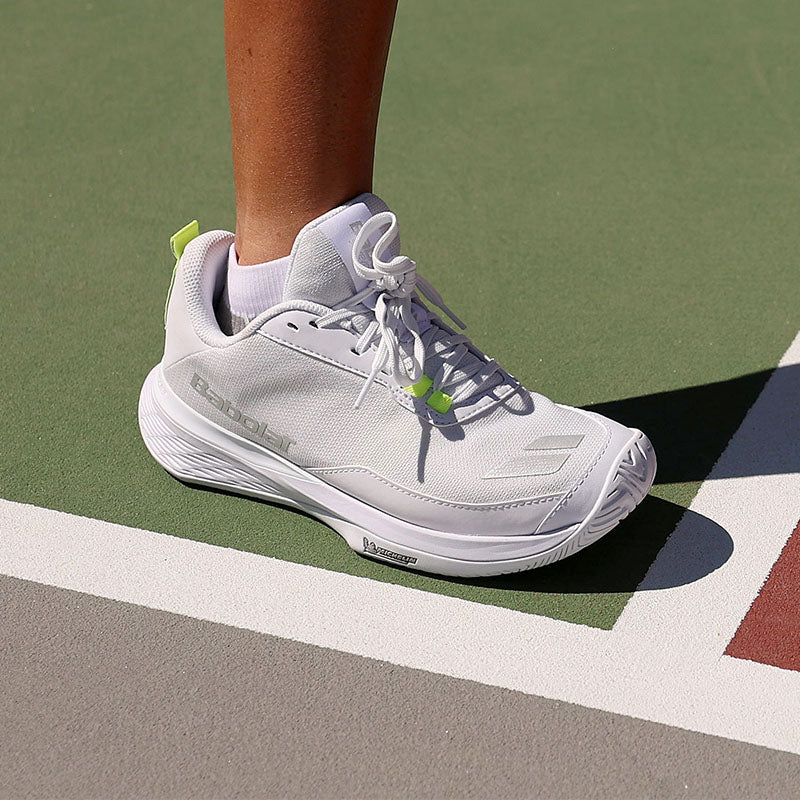 Person wearing white Babolat pickleball shoes with yellow accents on a court