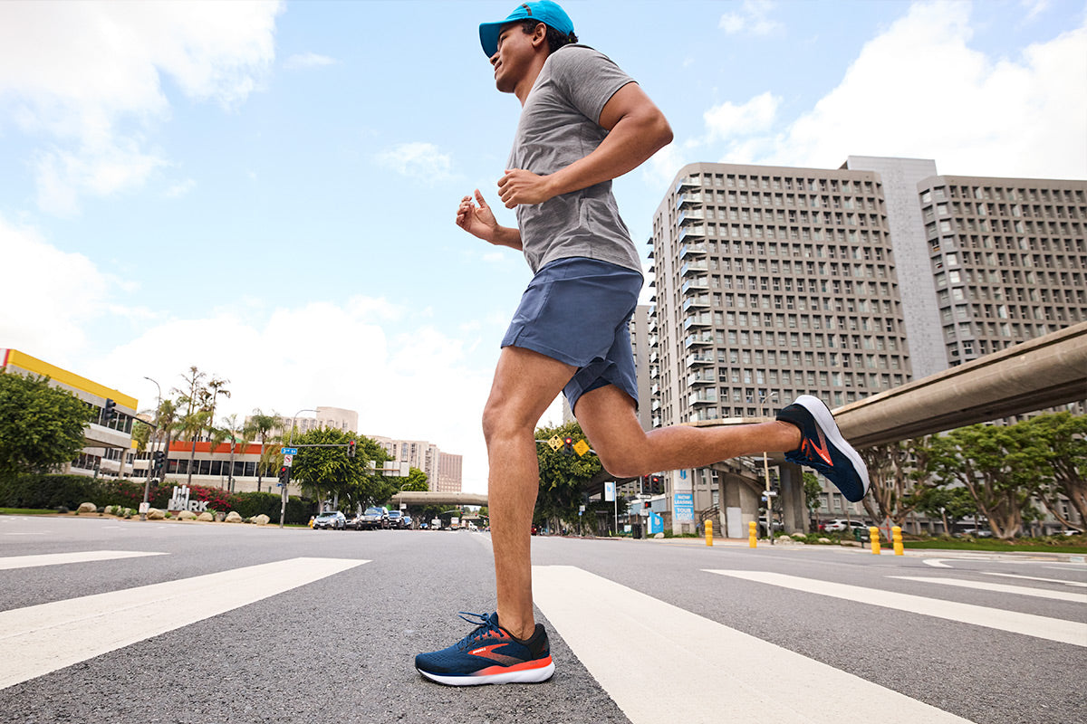 A man running down a city street, wearing the Brooks Ghost 16 shoes, characterized by their sleek design and optimal performance for urban runners.