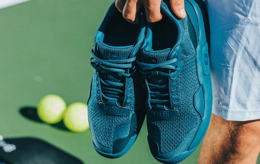 closeup of a person holding the Cypher Key211 pickleball shoes with a blurred pickleball court in the background