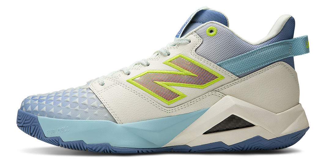 A blue and beige New Balance Coco CG2 Mid tennis shoe with lime green accents on a white background