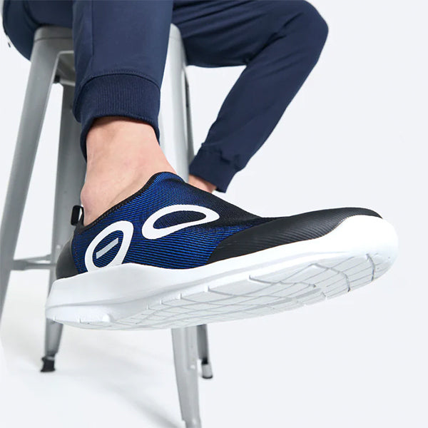 Closeup of a person wearing blue OOFOS OOmg Sport recovery walking shoes.