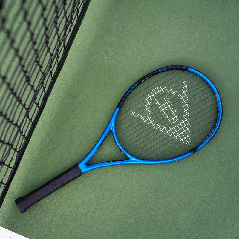 A blue and black Dunlop FX tennis racquet laying flat on a green tennis court.