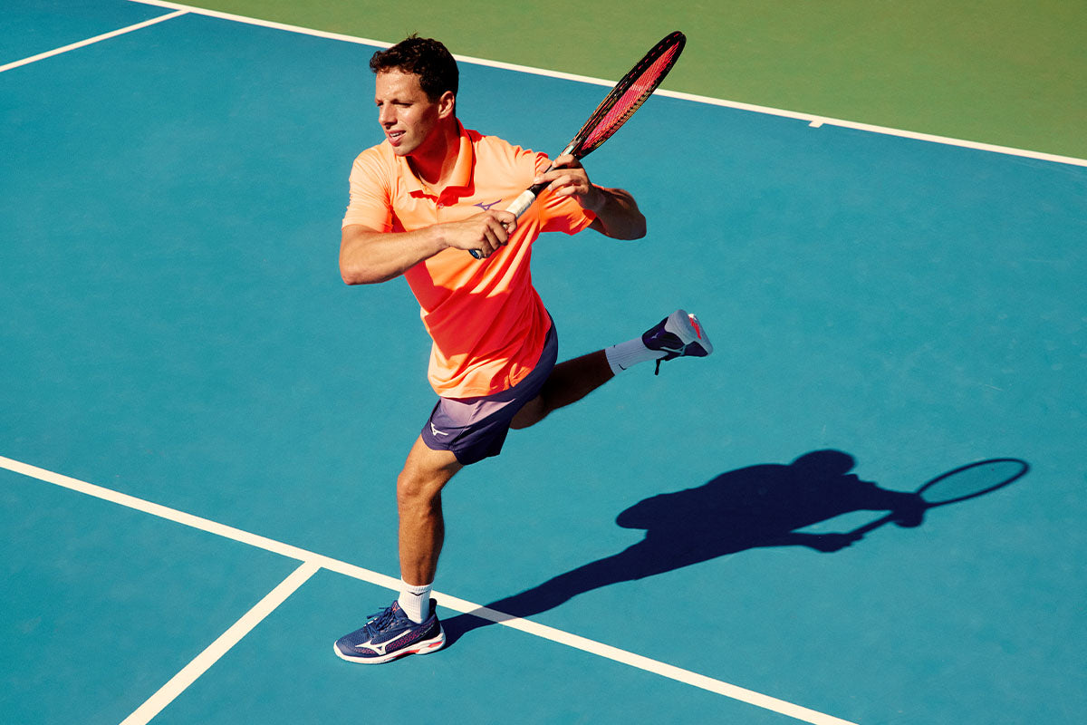 a tennis player on a blue court wearing men's mizuno tennis shoes and clothing