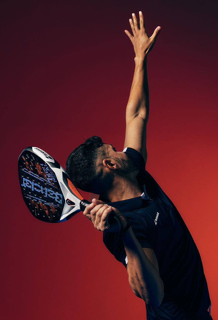 A man holding a Babolat Tecnical Viper padel racquet mid-serve against a red gradient background