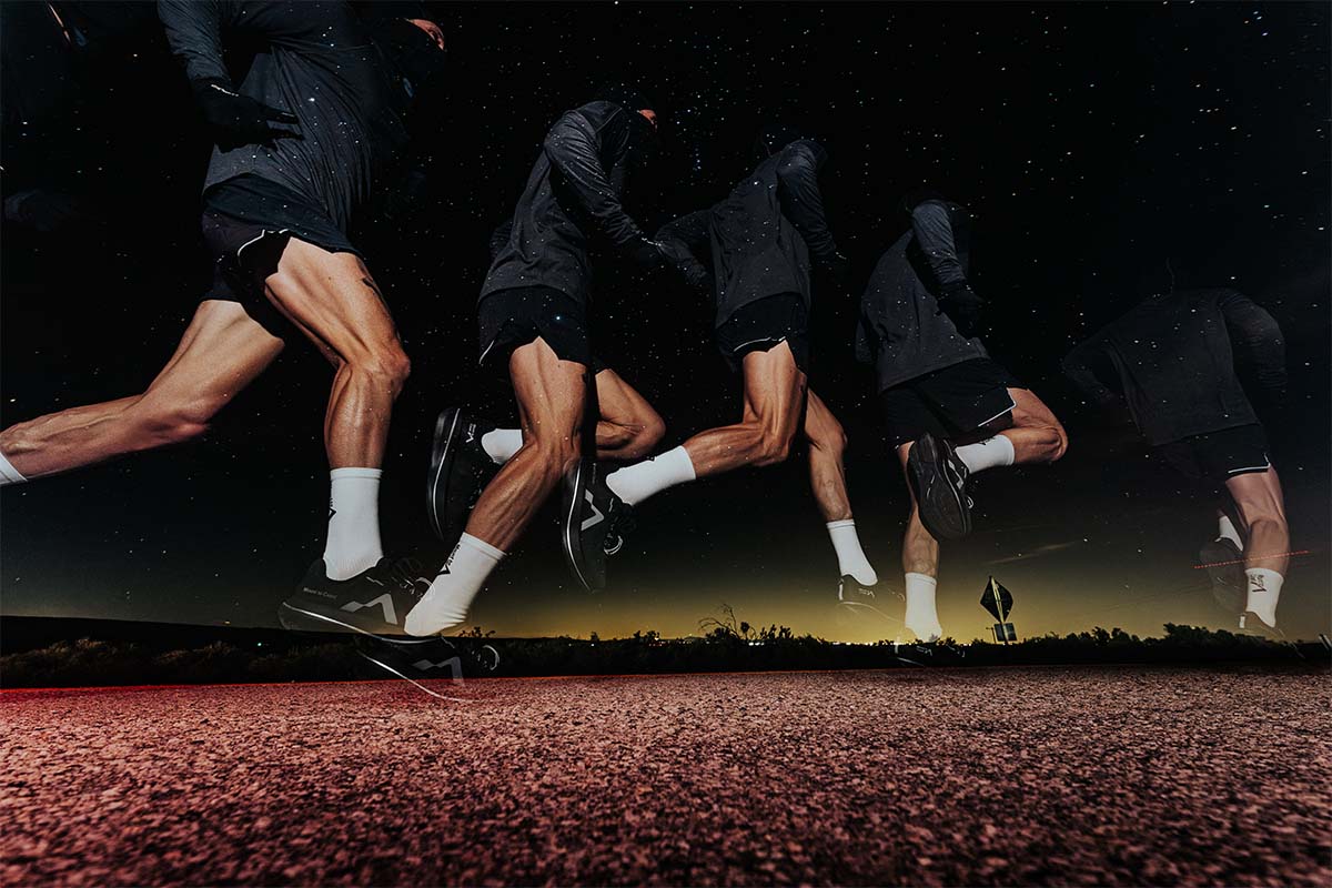 A person wearing black Mount to Coast C1 running shoes running on textured pavement against a night sky filled with stars and glowing light on the horizon