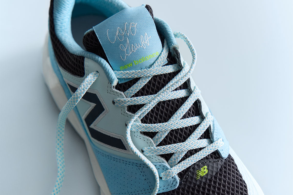 Light blue and black New Balance Coco Delray tennis shoe on a light blue background