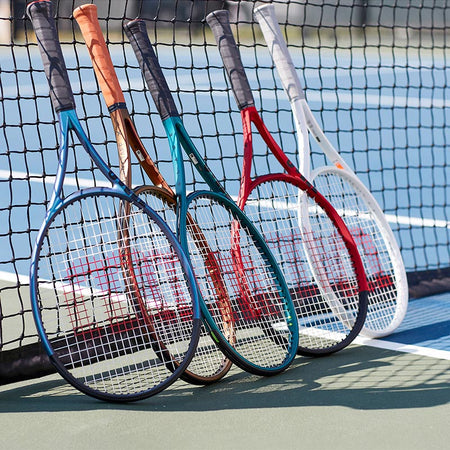 Wilson tennis racquets propped up against a net on a blue and green tennis court