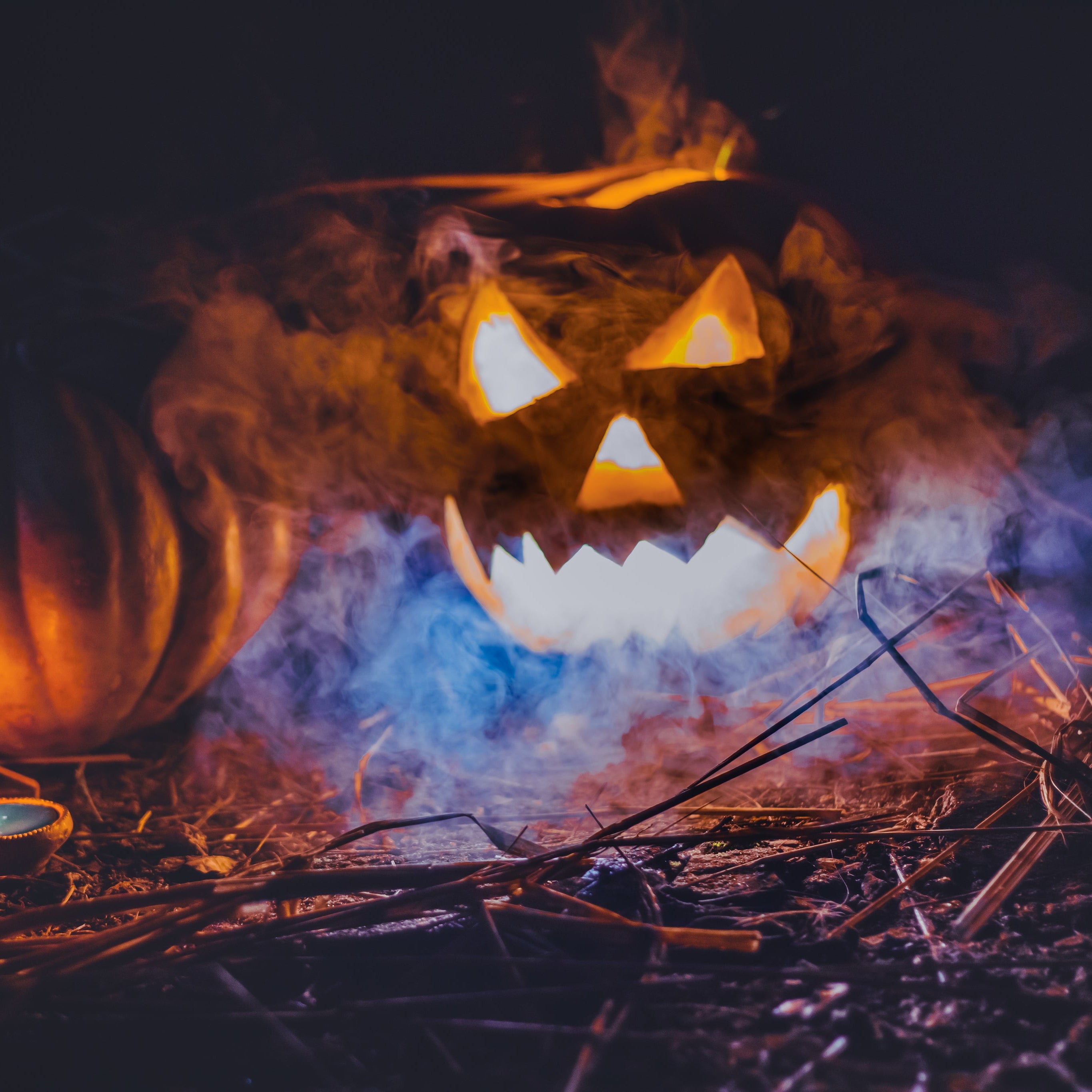A glowing jack-o-lantern and pumpkin on the ground with smoke
