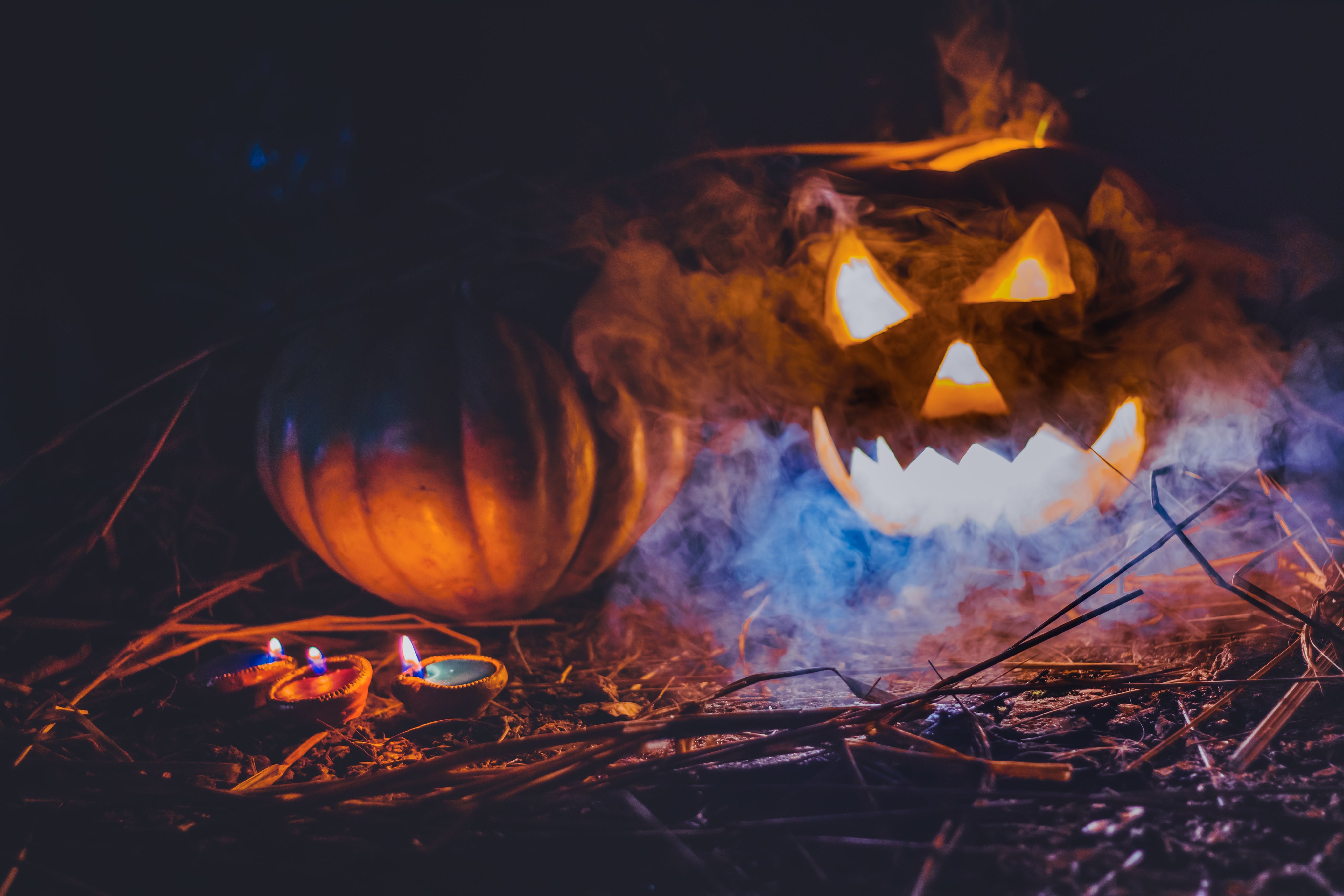 A glowing jack-o-lantern and pumpkin on the ground with candles and smoke