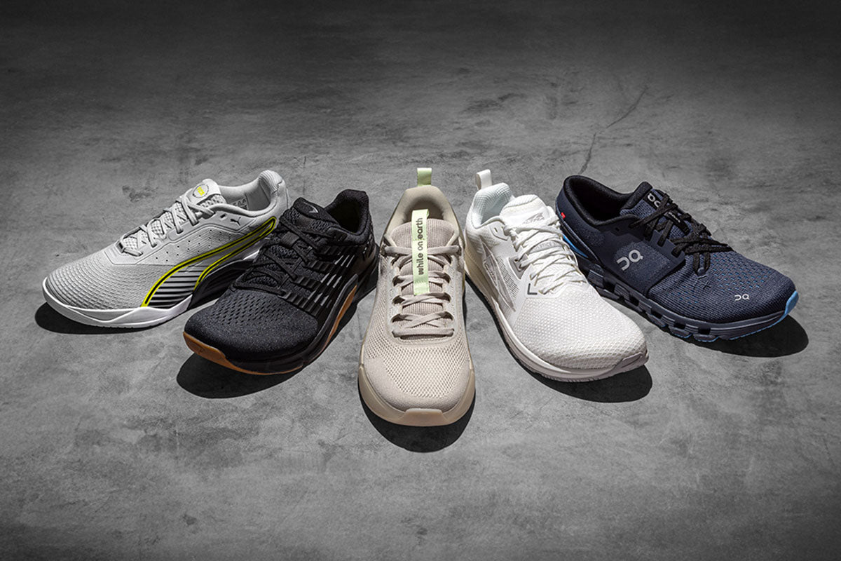 Five training shoes in various colors on a gray concrete surface