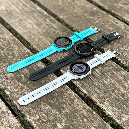 Teal, Black and White Garmin GPS 55 watches laying flat on a wooden dock.