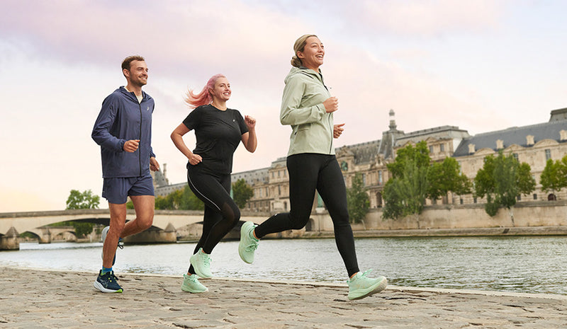 man and 2 women running in sics running shoes on cobblestone road along river