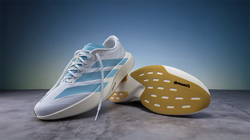 White and blue adidas Adizero EVO SL running shoes on a gray floor against a blue background
