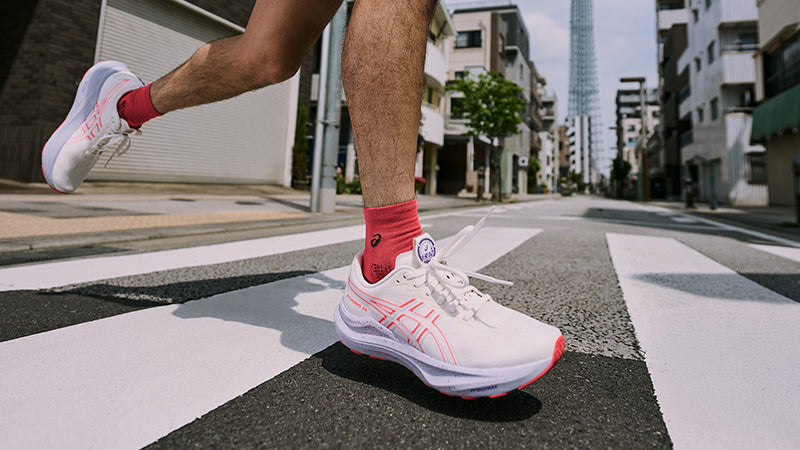 Person wearing white ASICS GT-2000 14 running shoes with pink accents on a city street.