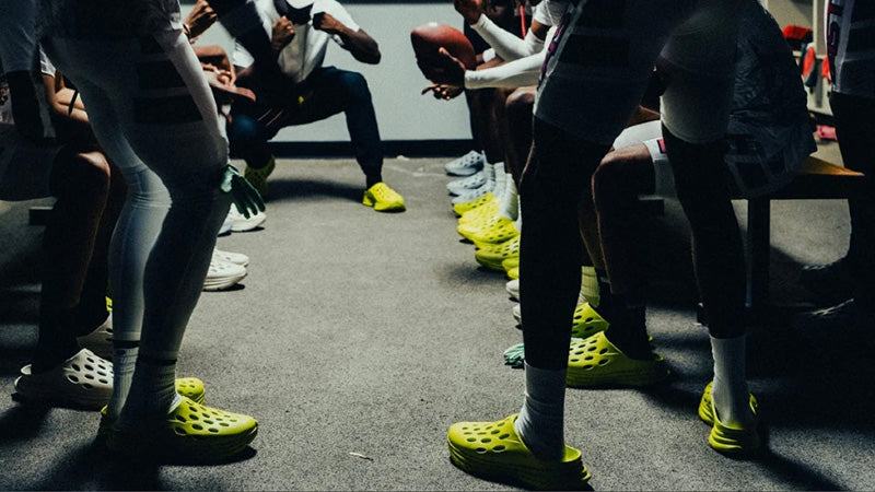Football players in a locker room all wearing Kane Revive OB recovery shoes