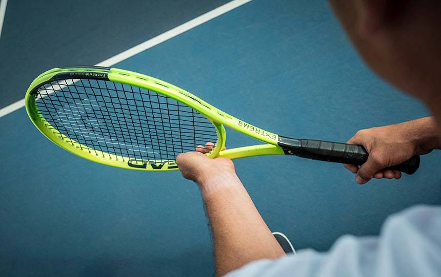 over-the-shoulder view of a tennis player holding a bright green HEAD Extreme 2026 tennis racquet over a blue court.