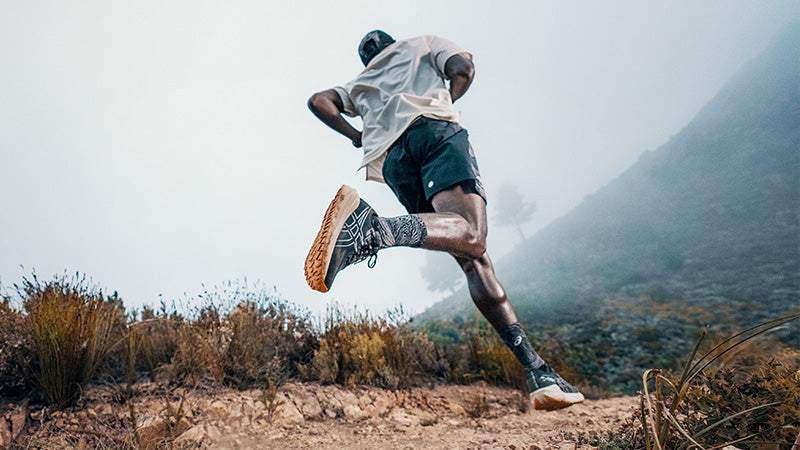 A trail runner wearing ASICS Blazeblast trail running shoes on a dirt trail in the foothills of a foggy terrain