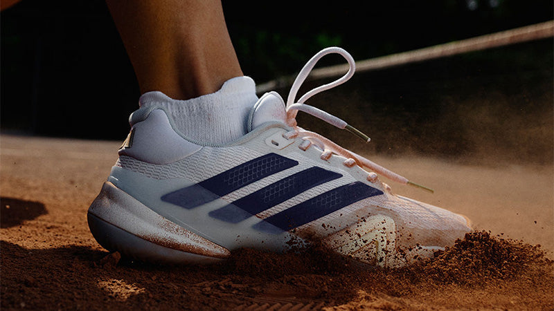Closeup of a tennis player wearing white adidas Barricade 14 women's tennis shoes with dark blue accents on a clay court