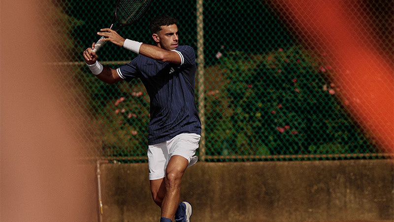 Tennis player in action wearing a dark blue adidas tee and white adidas shorts.