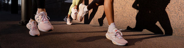 Three women running in adidas Solar Glide 5 White/Silver Metallic/Light Flash Orange running shoes.