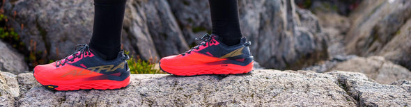 Man standing on a large rock in Altra Mont Blanc Coral/Black trail running shoes.