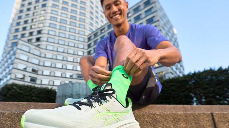 A man tying ASICS running shoes with a cityscape in the background