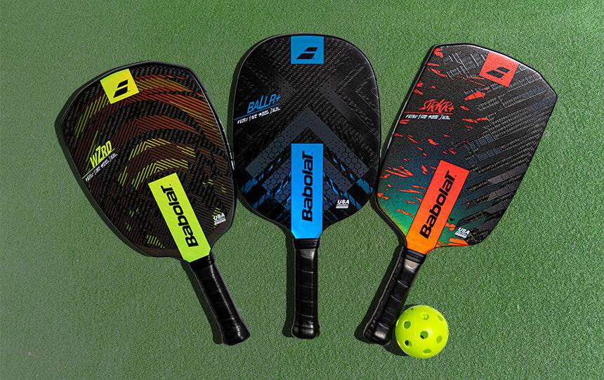 Babolat pickleball paddles and balls sitting on a green court