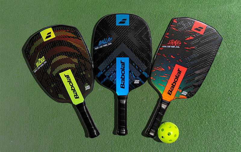 Babolat pickleball paddles and balls sitting on a green court