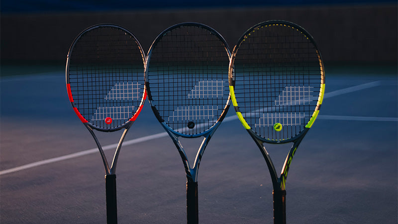 Babolat Pure Strike, Pure Drive and Pure Aero tennis rackets with different color schemes on a tennis court.