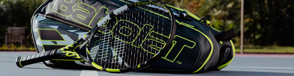 A Babolat Pure Aero 2023 tennis racquet leaning against a matching racquet bag on a blue tennis court.