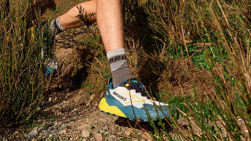 Person running on a rocky trail wearing Brooks Caldera 8 trail running shoes.