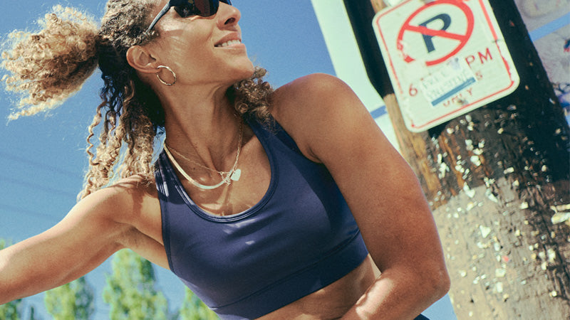 A runner wearing a Brooks Dash Bra and sunglasses next to a street pole