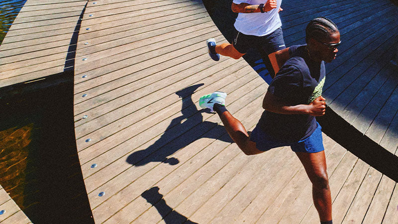 Two runners on a curved boardwalk wearing men's Brooks running shoes and clothing