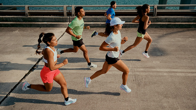 A man and a woman running in blue and yellow Brooks Run Within clothing against a golden yellow background.