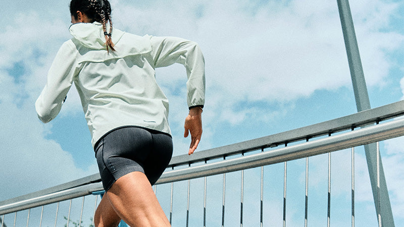 Person running by a metal railing against a clear blue sky wearing Brooks Women's Running Clothing