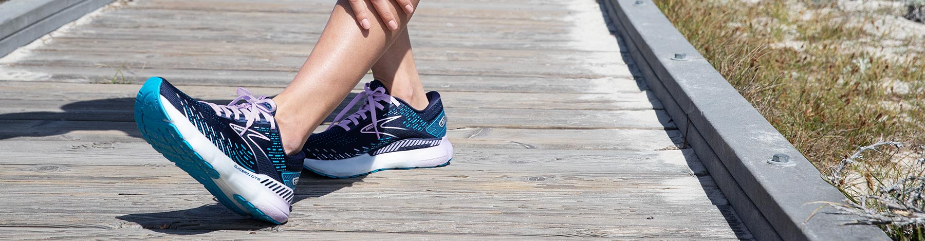 A person stretching their legs on a boardwalk in Brooks Glycerin GTS 20 running shoes.