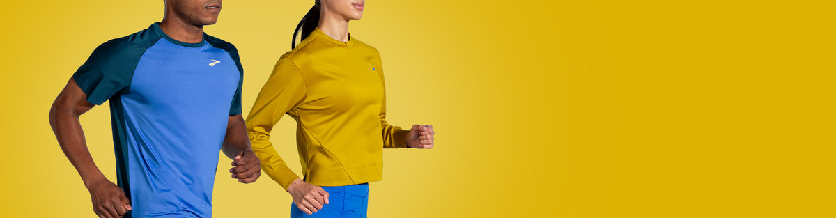 A man and a woman running in blue and yellow Brooks Run Within clothing against a golden yellow background.